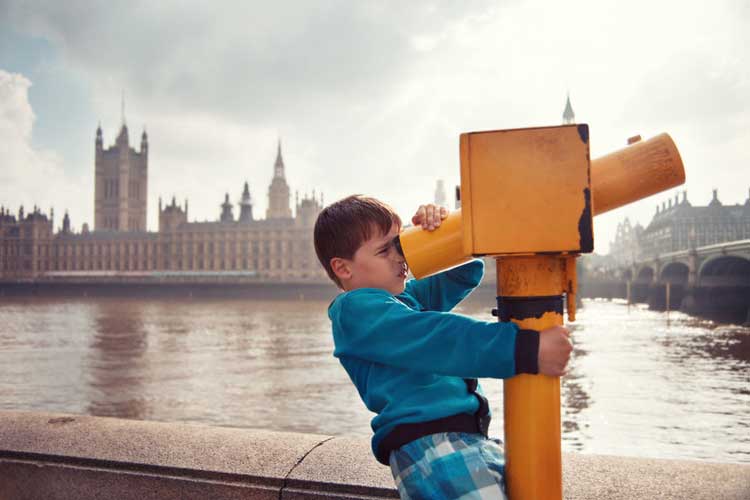 A boy looking through a telescope with the Houses of Parliament in the background.