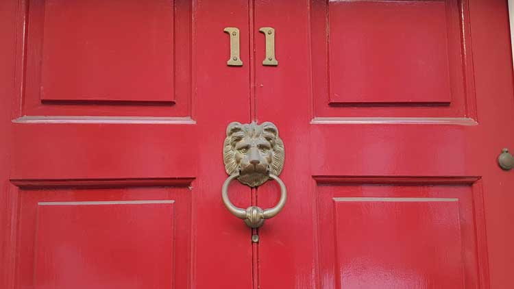 A red door with a lion's head doorknocker on it.